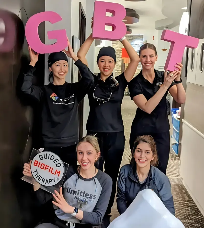 Team members holding pink letters spelling GBT and a Guided Biofilm Therapy sign